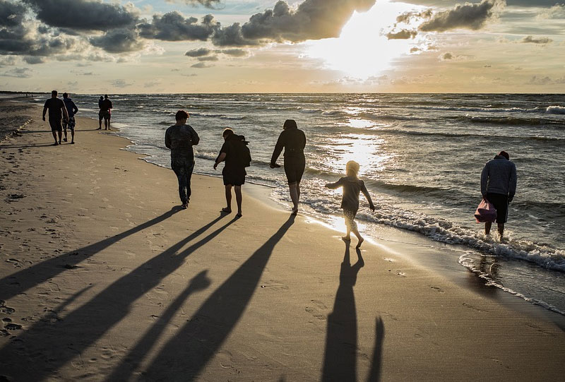 Image: A family walking along a beach at sunset.